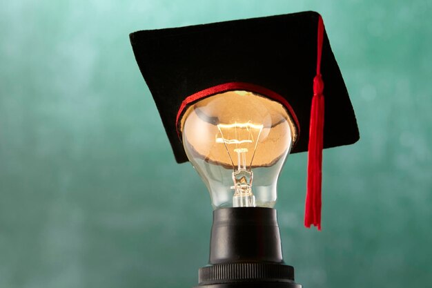 Photo close-up of mortarboard on illuminated light bulb against blue background