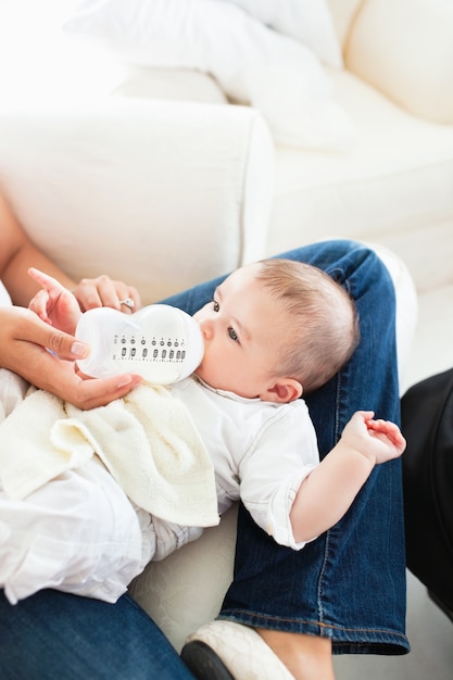 Close-up of a mother giving milk to her baby sitting in the couch