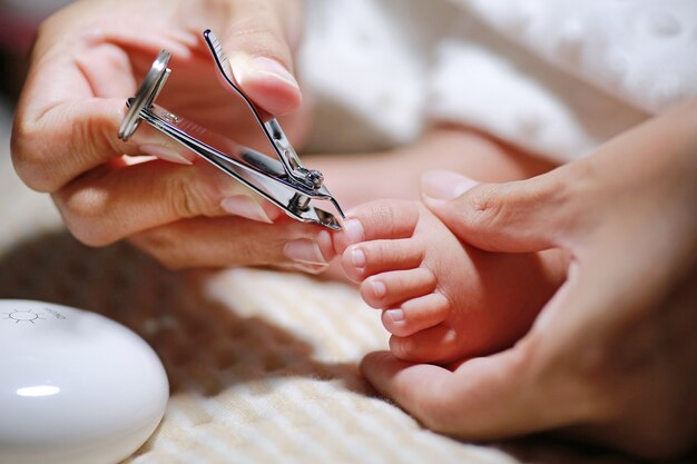 Photo close up mother hands cutting baby toenails.
