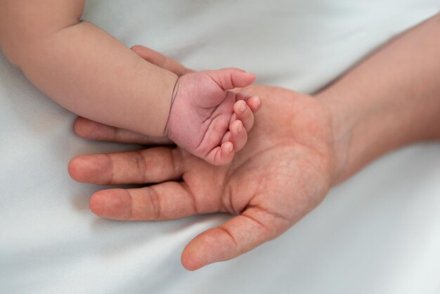 Primo piano madre che si tiene per mano neonato in una stanza con molta luce solare bambino