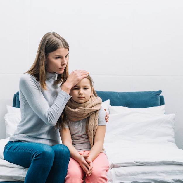 Foto primo piano di una madre che tocca la fronte di sua figlia che soffre di febbre