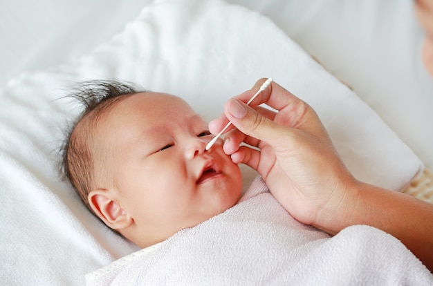 Close-up mother use cotton bud to clean infant nose. Baby Healthcare concept.