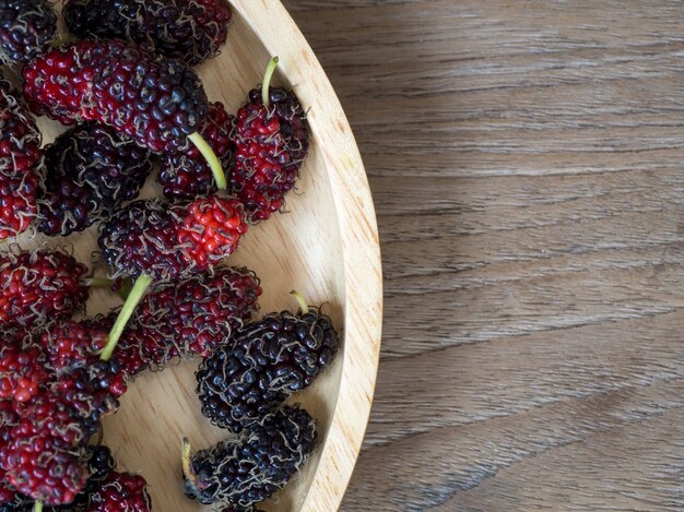 Close up of mulberry with a green leaves on the wooden plate on wooden table.