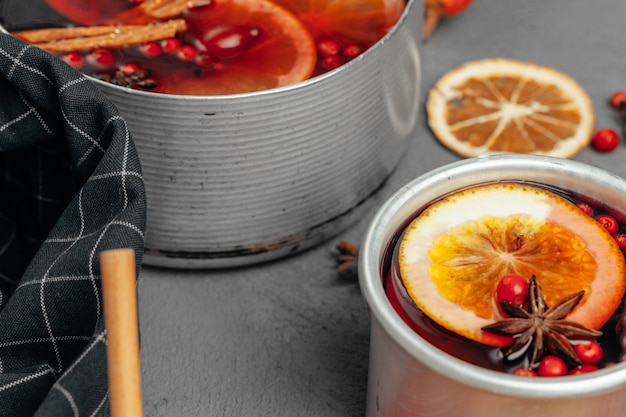 Close up of mulled wine cup with spices and berries on grey table