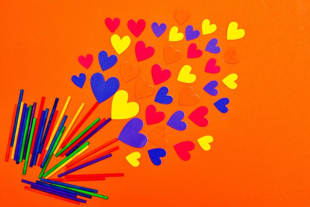 Close-up of multi colored straws and heart shapes against orange background