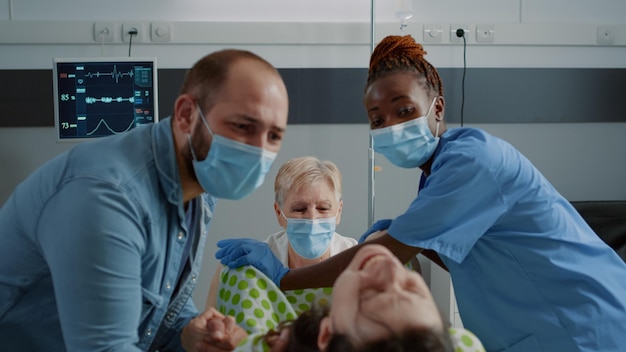 Close up of multi ethnic people delivering child in hospital ward. Doctor and african american nurse helping pregnant woman pushing for childbirth. Caucasian husband holding wife hand