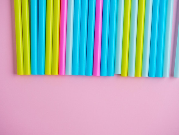 Close-up of multicolored plastic tubes on a pink paper background. Top view, flat lay