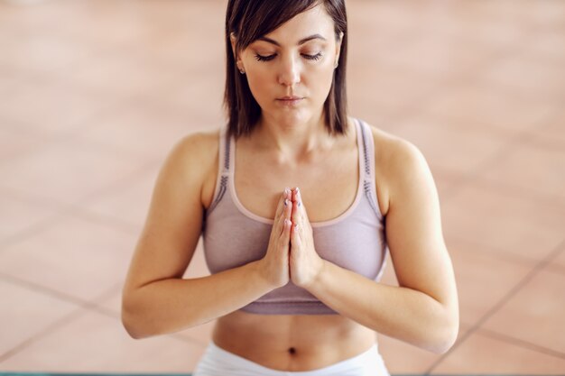 Close up of muscular young brunette sitting in lotus position and meditating.