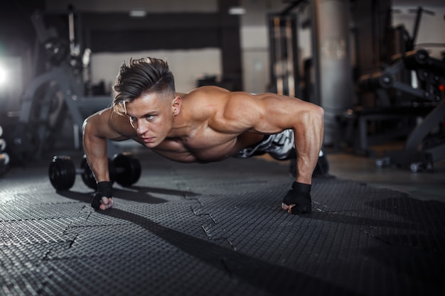 Close Up of a muscular young man lifting weights in gym on dark background. High quality photo