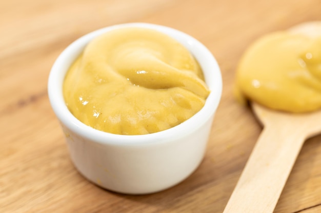 Photo close up of mustard sauce in bowl and spoon on wooden table