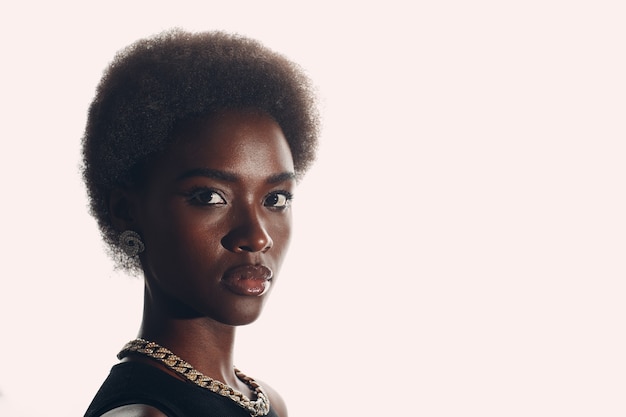 白いスタジオの背景にアフロの髪型を持つアフリカ系アメリカ人女性の自然な肖像画を閉じます。