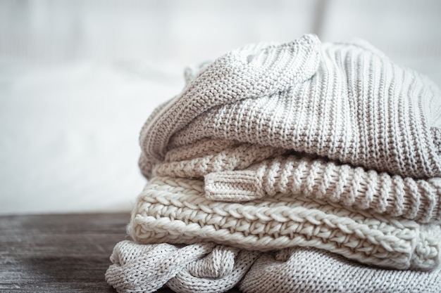 Close up of neatly folded knitted items of pastel color on a light background.