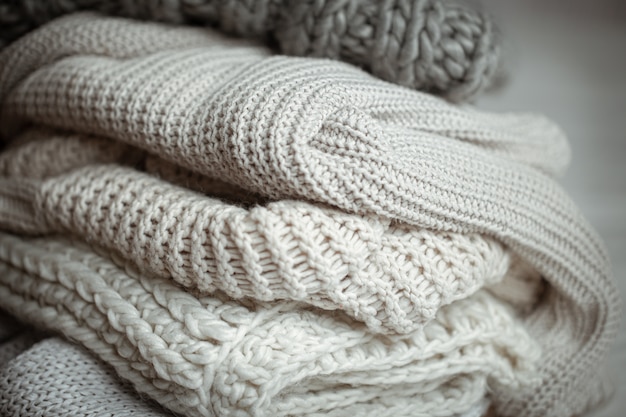 Close up of neatly folded knitted items of pastel color on a light background.