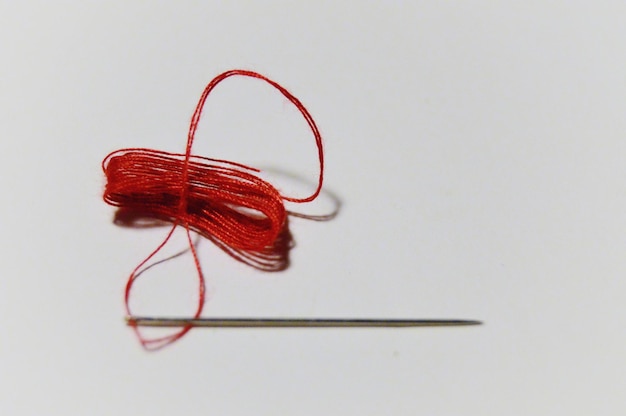 Photo close-up of needle with red thread over white background