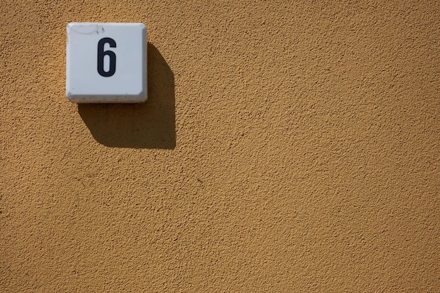 Foto close-up del numero 6 sul muro di cemento giallo durante una giornata di sole