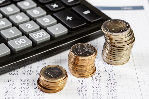 Фото Крупный план калькулятора и трех стопок монет на деловом фоне