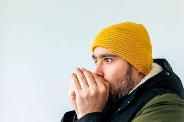 灰色の壁の背景のスタジオで隔離のポーズの冬のコートで凍った若いひげを生やした男のクローズアップ