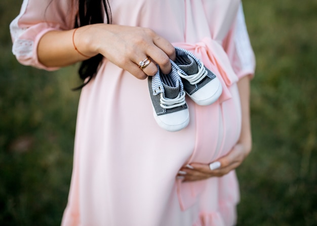 写真 彼女の腹に小さな赤ちゃんの靴を持っている妊婦のクローズアップ
