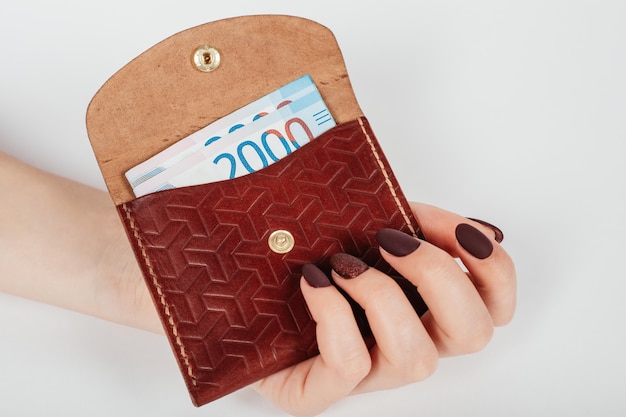 Фото Крупным планом - руки женщины кладут в кошелек банкноту в тысячи рублей.