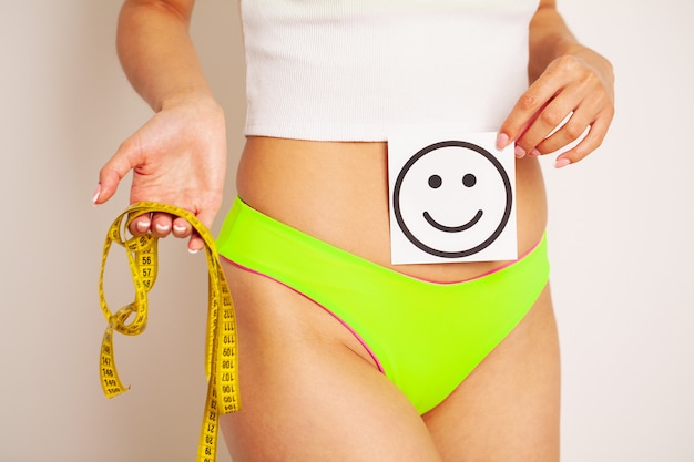 写真 細身の女性のクローズアップは、笑顔と黄色のメジャーテープで彼女の胃の近くでカードを保持している結果を示しています。