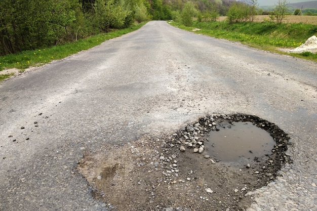 Фото Закройте вверх большой выбоины с пакостной дождевой водой дороги.