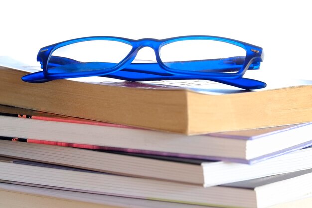 Фото Близкий взгляд на голубые очки на сложенных книгах на белом фоне