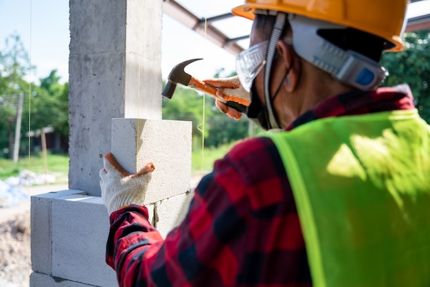 벽돌공 빌더의 클로즈업은 해머를 사용하여 고압 증기 멸균 콘크리트 블록을 도와줍니다. 벽, 건설 현장에 벽돌 설치