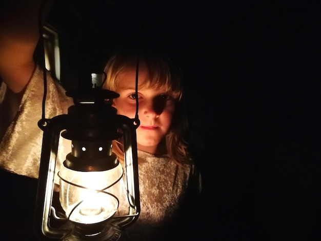 写真 暗室で照らされたオイルランプを持った女の子のクローズアップ