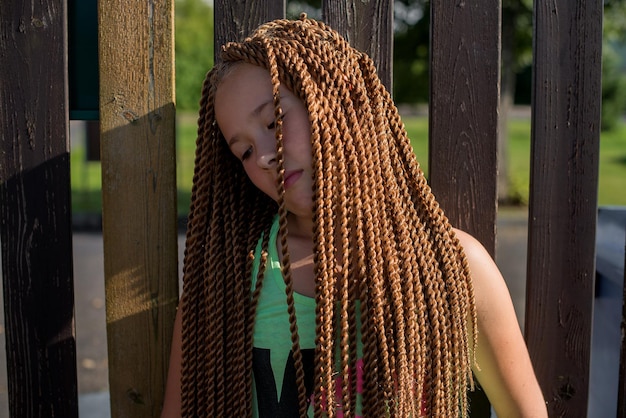 写真 木製のフェンスに立っているドレッドロックの女の子のクローズアップ