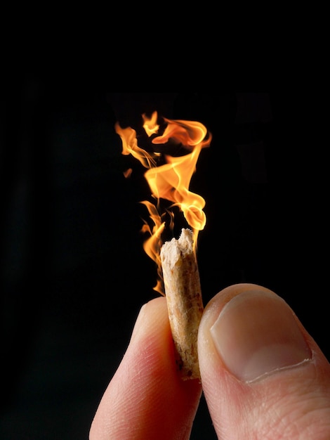 Фото Близкий план руки, держащей горящую древесную гранулку на черном фоне