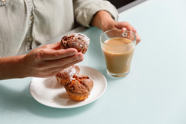 写真 カードマフィンとミルクのあるグラスカップのコーヒーを握った手を近づける