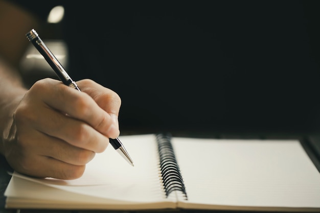 写真 木製のテーブルの上のノートに書くペンを持つ男性の手のクローズアップ
