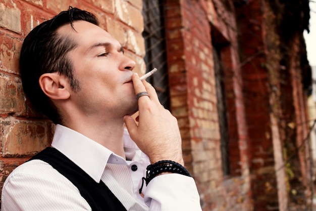 写真 レンガの壁に寄りかかってタバコを吸っている男のクローズアップ