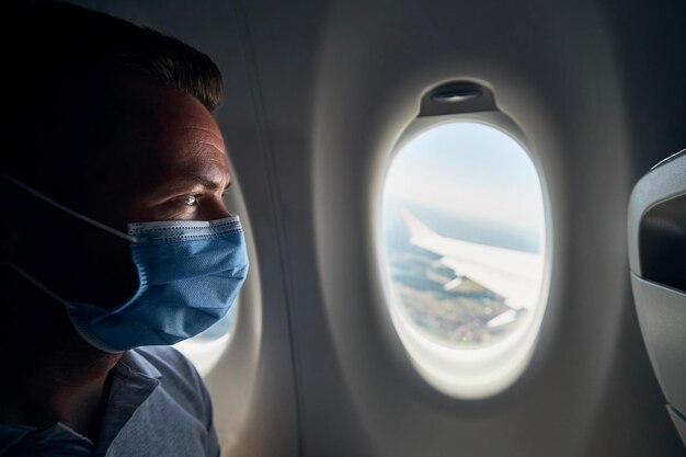 사진 독감 마스크를 착용 한 남자가 비행기에 앉아있는 클로즈업