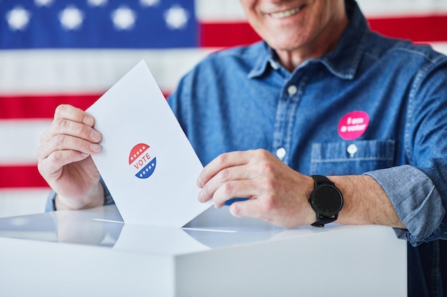 사진 배경 복사 공간에 있는 미국 국기에 반대하여 투표지를 빈에 넣는 웃고 있는 노인의 클로즈업