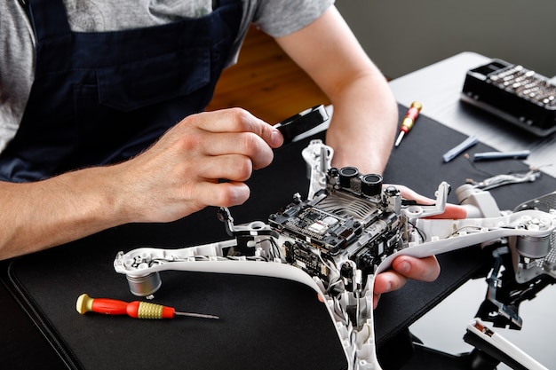 Фото Крупный план руки человека, ремонтирующего дрон с помощью отвертки. мужчина работает в ремонтной мастерской