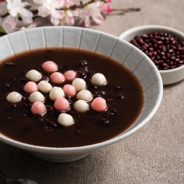 사진 동지 축제 음식을 위해 회색 테이블 배경에 있는 그릇에 달콤한 팥 수프와 함께 빨간색과 흰색 탕위안(탕 위안, 찹쌀 만두 공)을 닫습니다.