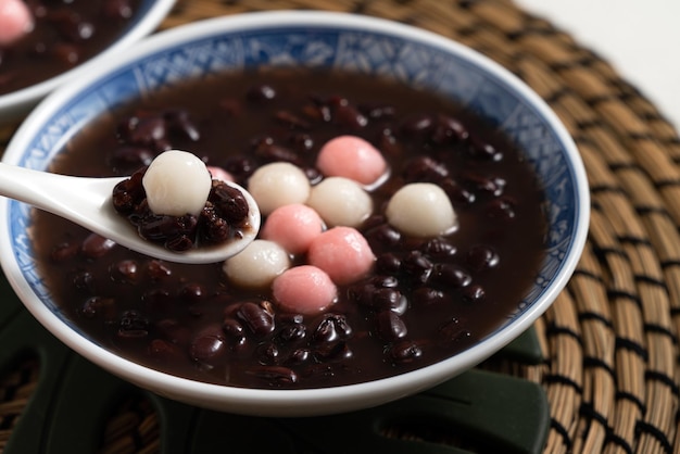 冬至の祭りの食べ物のための白いテーブルの背景にボウルに甘い小豆のスープで赤と白の湯円（湯円、もち米団子ボール）のクローズアップ。