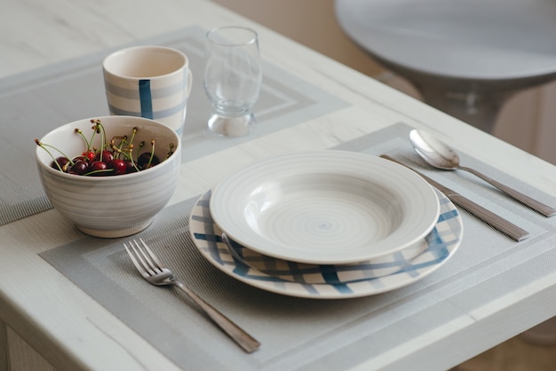 Фото Крупный план поданной обеденной тарелки, ножа, ложки и вилки, чашки и стакана и вазочки с вишнями на обеденном столе