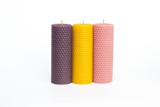 Закройте набор из трех фиолетовых, желтых и розовых декоративных свечей из натурального пчелиного воска с медовым ароматом для интерьера, изолированные на белом фоне