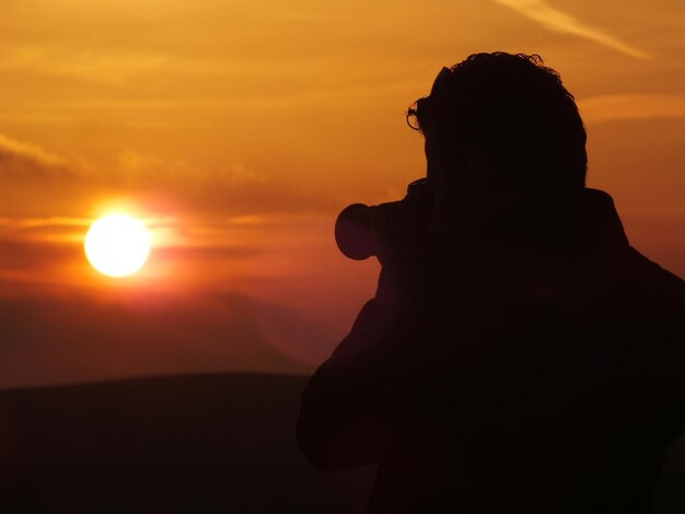 写真 夕暮れの空を撮影するシルエット男のクローズアップ