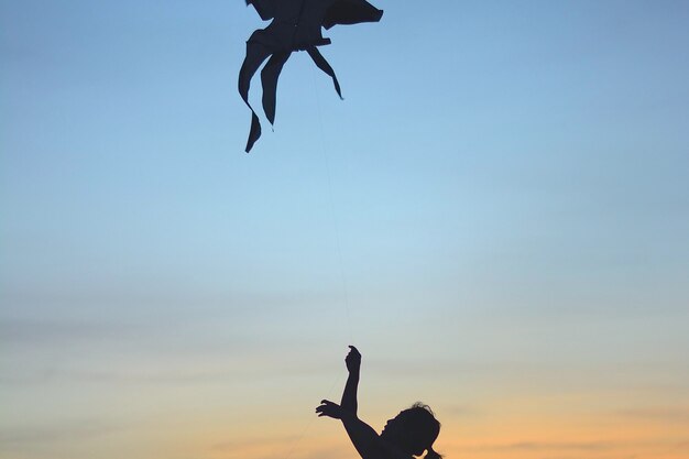 사진 해가 지는 동안 하늘을 향해 kite를 날리는 실루 여성의 클로즈업