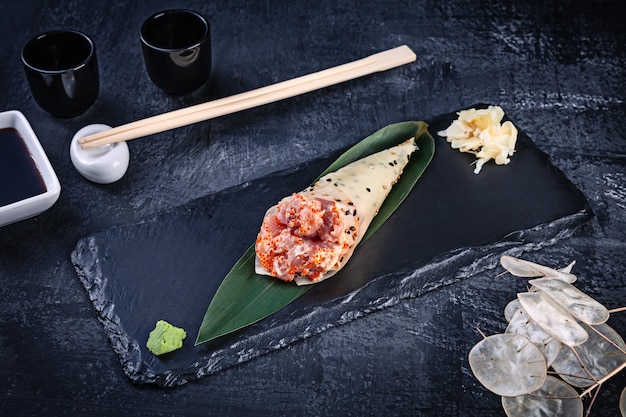 Крупным планом вкусные суши ролл руки в mamenori с тунцом и икрой тобико, подается на темной каменной плите с соевым соусом и имбирем. копировать пространство темаки, японская кухня. здоровая пища