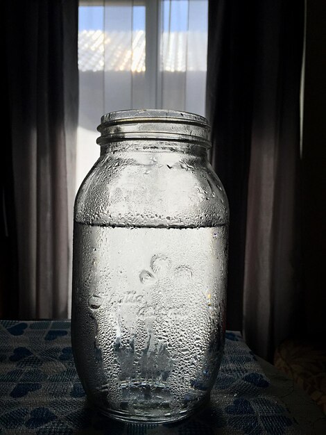 Фото Клоуз-ап воды в стеклянной банки на столе напротив окна дома