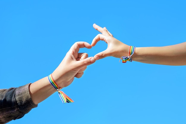 Фото Крупным планом женские руки в радужном браслете, делающем форму сердца на фоне голубого неба