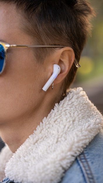 사진 여성의 클로즈업은 귀에 넣고 제어하기 위해 손으로 흰색 진정한 무선 이어폰을 사용하고 있습니다