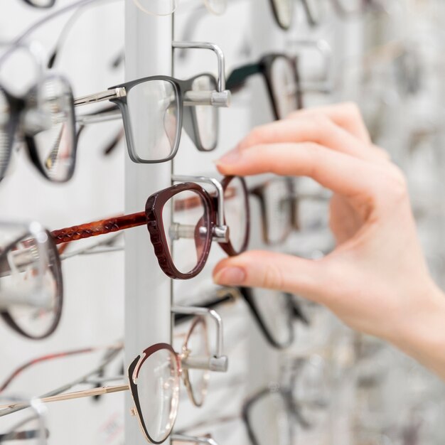 Крупный план женской руки выбирает очки в магазине оптики
