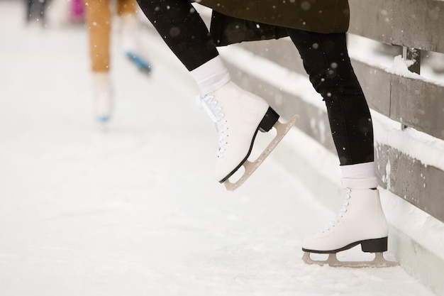 Фото Закройте вверх ног конькобежца женщины на открытом катке, взгляде со стороны. женские белые коньки на льду, тренируются у стены, учатся балансировать. выходные мероприятия на свежем воздухе в холодную погоду.