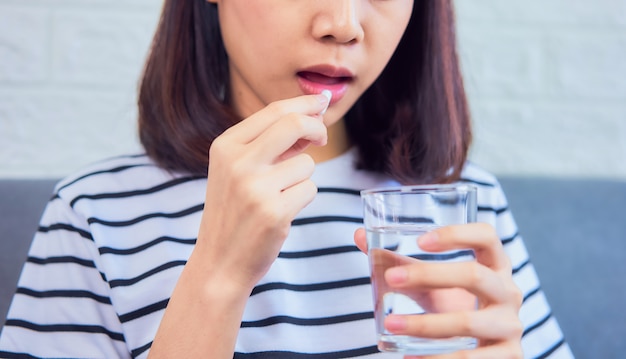 写真 口の中で白い錠剤を服用し、家のソファーにガラスの水を飲む女性のクローズアップ