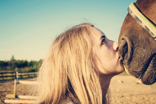Фото Клоуз-ап молодой женщины, целующей лошадь на чистом небе.